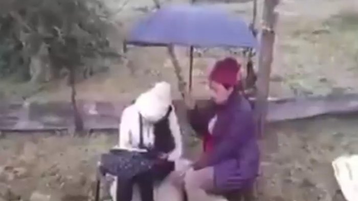 Estudiante asiste a clases online bajo la lluvia: Su mamá sostiene un paraguas para que no se moje